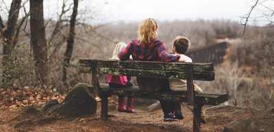 白天坐在棕色木凳上的两个孩子中间的女人